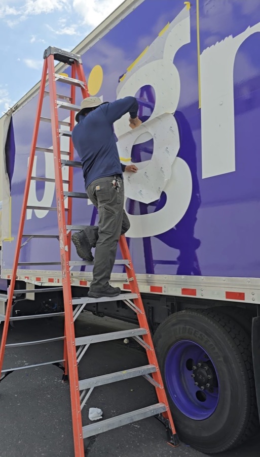 Installer on a ladder pressing a large white vinyl letter into place