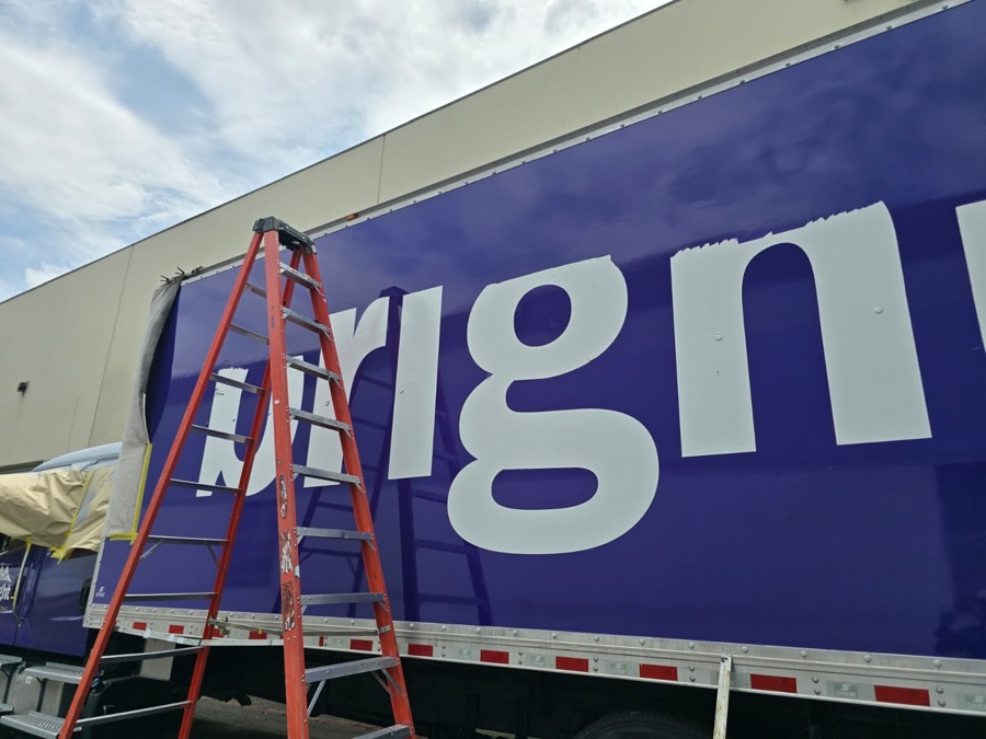 Large white vinyl lettering going onto the side of a purple box truck