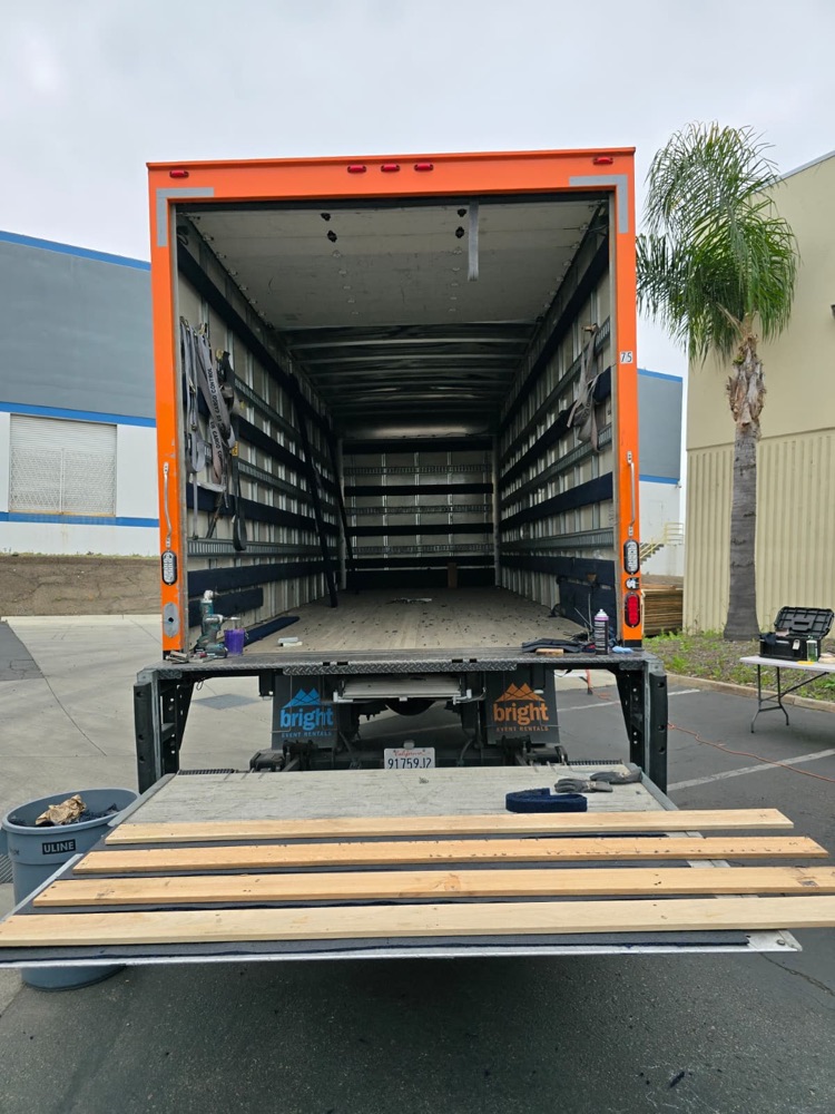 Open orange box truck with E-track rails and wood slats installed along the inside walls and a liftgate with lumber on it