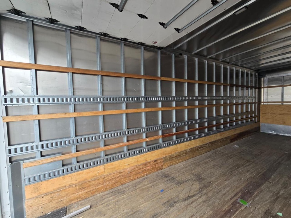 Inside wall of the box truck with three rows of E-track and wood slats fitted between the wall posts