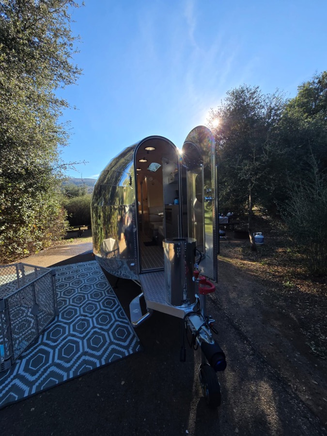 Polished aluminum travel trailer with its door open at a customer site
