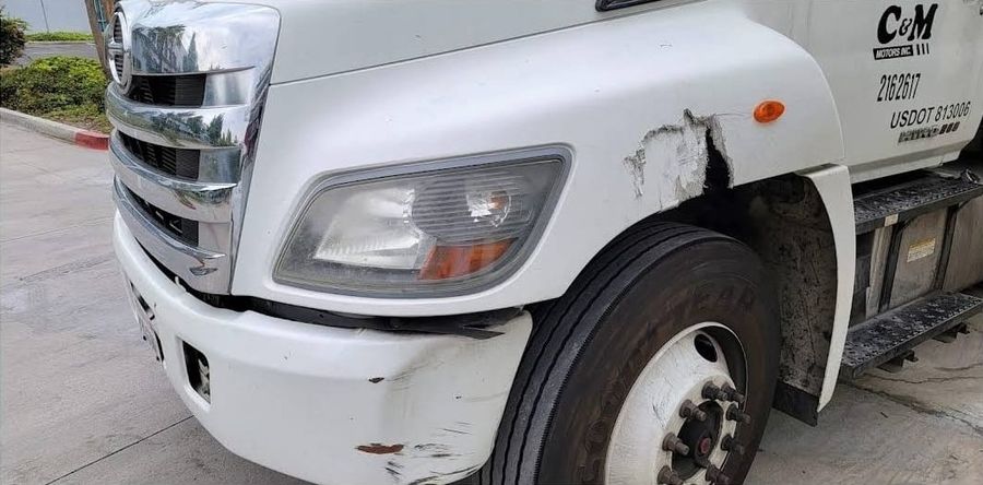 White Hino truck with a cracked fender and scraped bumper