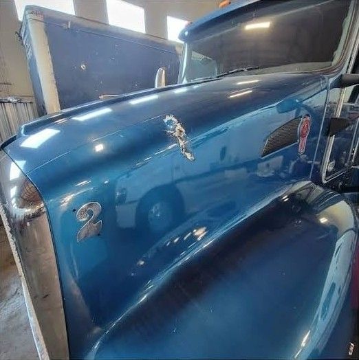 Blue Kenworth hood with chipped and peeling paint around the emblem