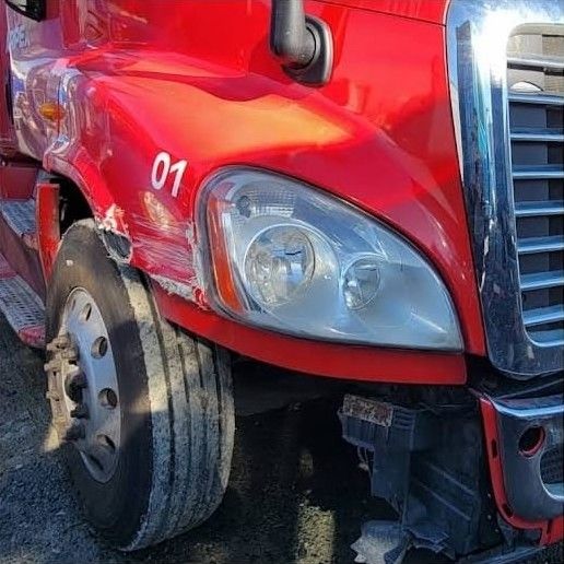 Red Freightliner tractor with a scraped fender and damaged bumper corner