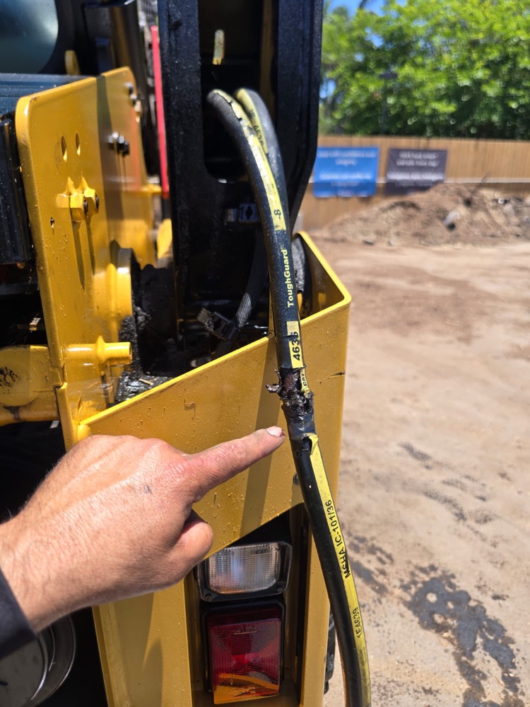 Cat skid steer with a burst hydraulic hose, the torn spot pointed out by hand