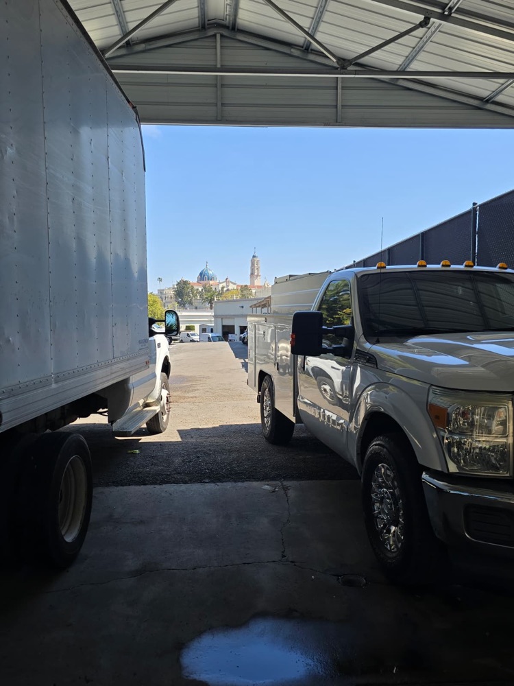 White box truck parked next to a white service truck under a metal canopy