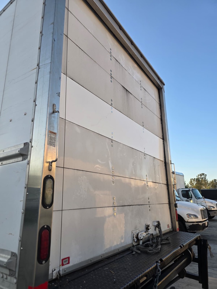 Rear roll-up door of a box truck with one new white panel replaced