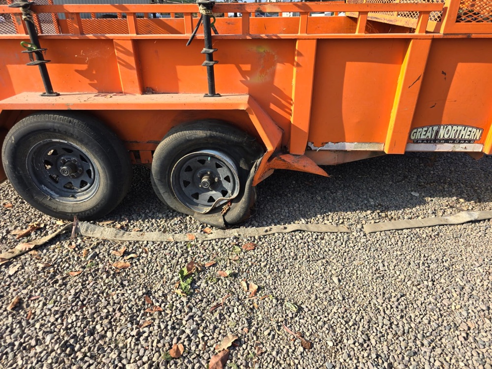 Orange utility trailer with a crushed fender and a destroyed tire