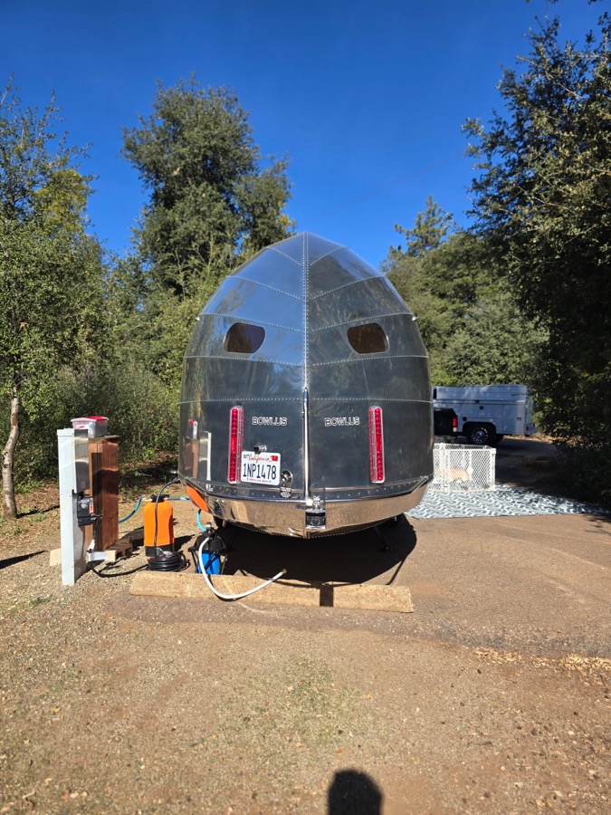 Polished aluminum travel trailer from behind, parked at a customer site